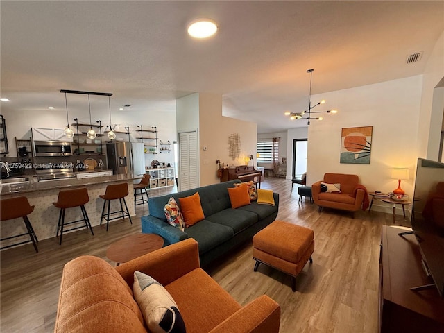 living room featuring light wood-style floors, visible vents, and an inviting chandelier