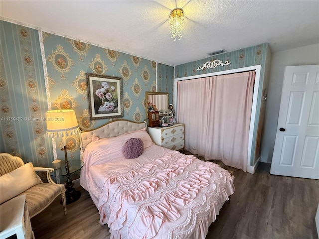 bedroom with wallpapered walls, visible vents, wood finished floors, a textured ceiling, and a closet