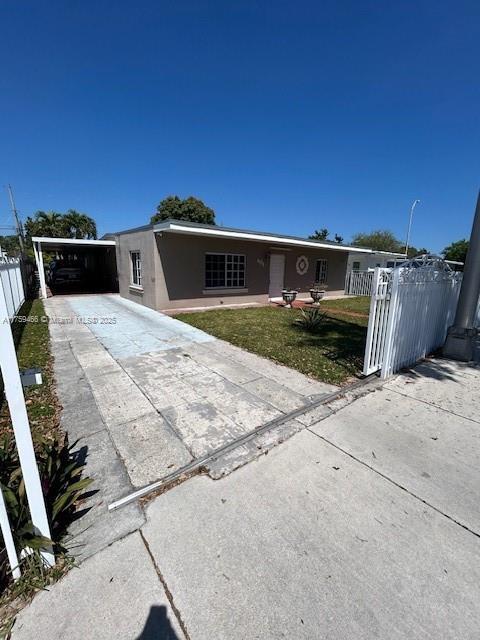 view of front of house featuring fence, concrete driveway, stucco siding, a carport, and a front yard