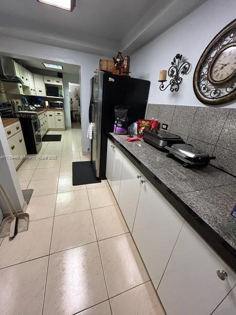 kitchen featuring light tile patterned floors, dark countertops, freestanding refrigerator, and white cabinets