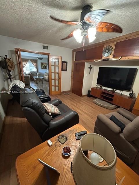 living room featuring light wood finished floors, a ceiling fan, visible vents, and a textured ceiling