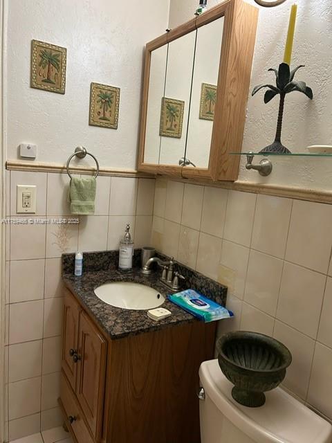 bathroom featuring toilet, tile walls, and vanity