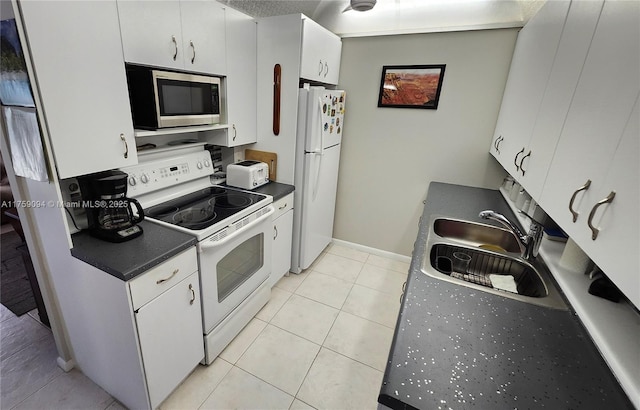 kitchen featuring white appliances, white cabinets, dark countertops, a sink, and light tile patterned flooring