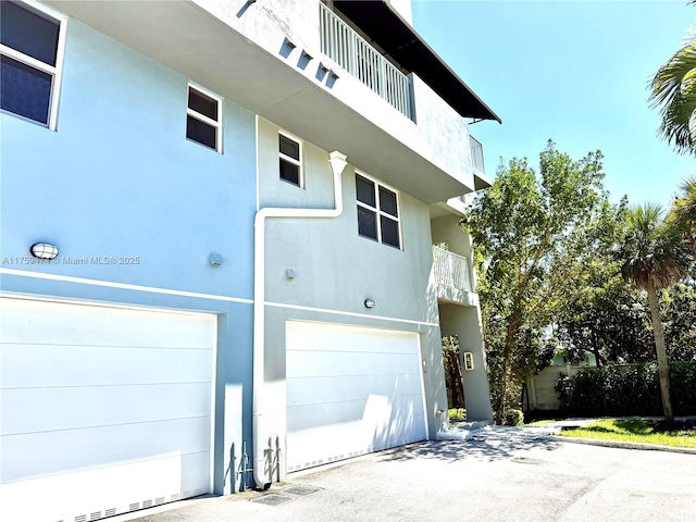 view of property exterior featuring an attached garage, a balcony, and stucco siding