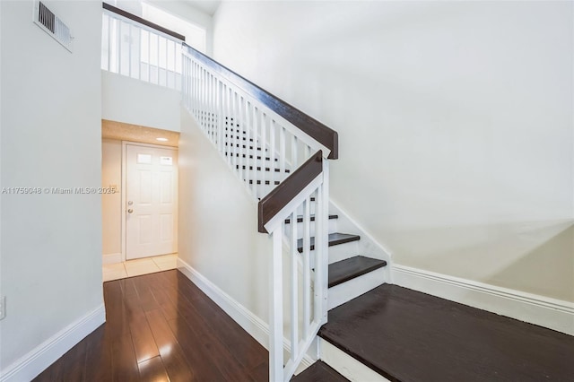 stairs featuring a high ceiling, wood finished floors, visible vents, and baseboards