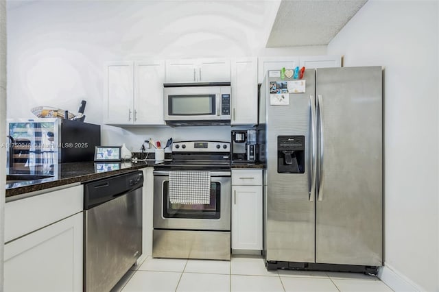 kitchen featuring light tile patterned floors, stainless steel appliances, dark stone counters, and white cabinetry