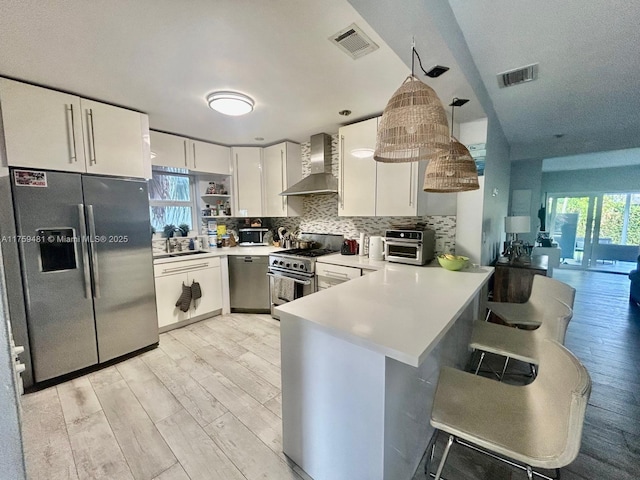 kitchen with stainless steel appliances, a peninsula, light countertops, wall chimney range hood, and decorative backsplash