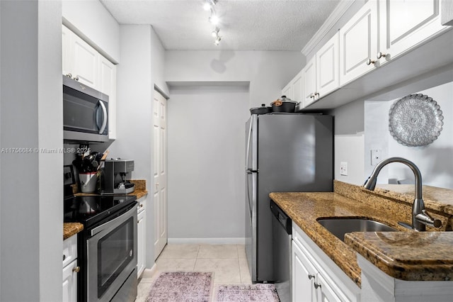 kitchen featuring appliances with stainless steel finishes, white cabinets, a sink, a textured ceiling, and dark stone countertops