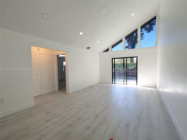 empty room featuring high vaulted ceiling, light wood-type flooring, a textured ceiling, and baseboards