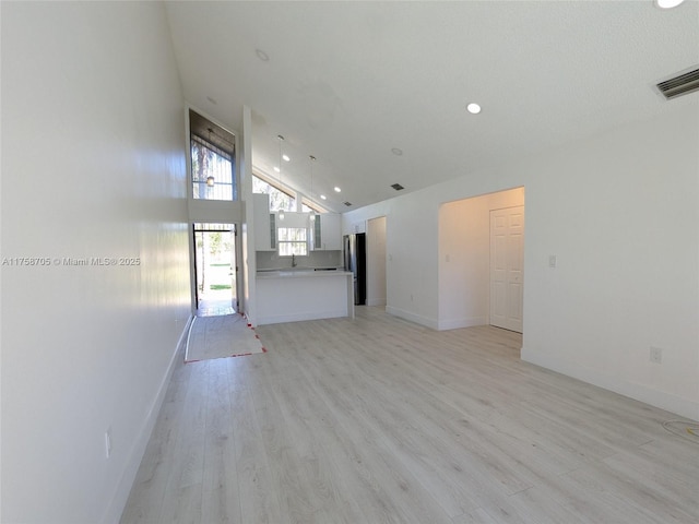 unfurnished living room with light wood finished floors, baseboards, visible vents, high vaulted ceiling, and recessed lighting