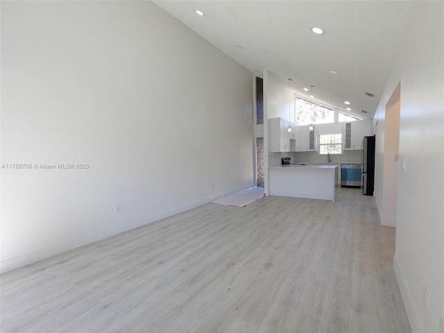 unfurnished living room with light wood-style floors, recessed lighting, high vaulted ceiling, and baseboards