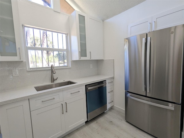 kitchen featuring dishwashing machine, a sink, white cabinets, freestanding refrigerator, and decorative backsplash