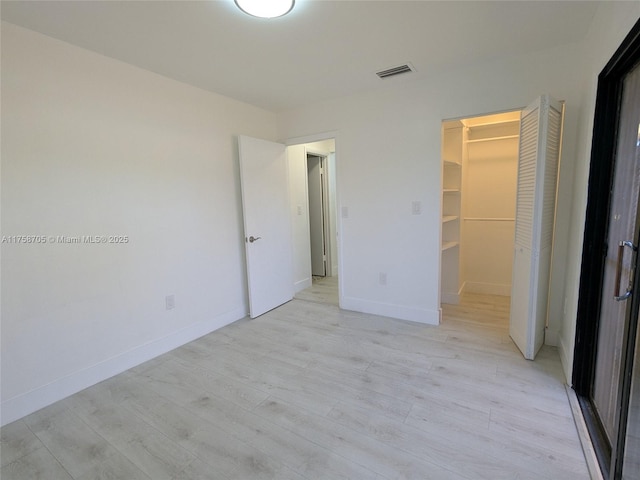 unfurnished bedroom featuring light wood finished floors, a walk in closet, visible vents, and baseboards