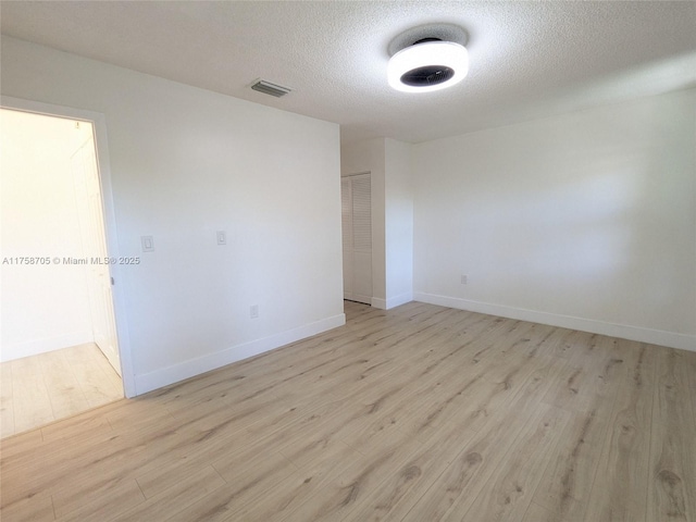 empty room featuring baseboards, visible vents, light wood-style flooring, and a textured ceiling