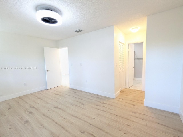 unfurnished room featuring light wood-type flooring, visible vents, a textured ceiling, and baseboards