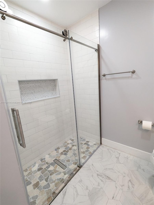 bathroom with toilet, marble finish floor, a shower stall, and baseboards