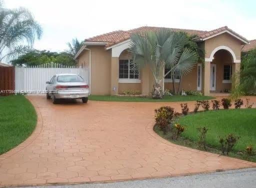 view of side of home with stucco siding, a tile roof, fence, a yard, and concrete driveway