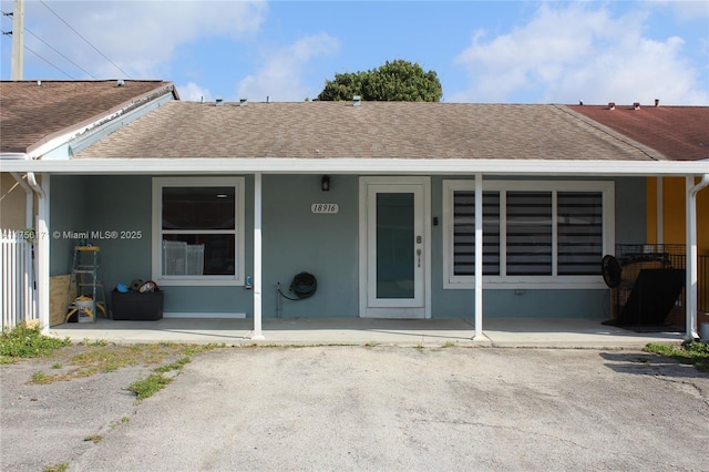 exterior space with covered porch, roof with shingles, and stucco siding