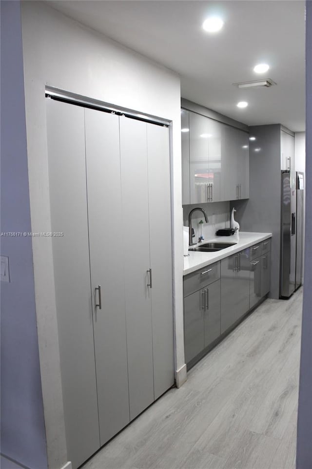 kitchen featuring gray cabinets, a sink, light countertops, light wood-style floors, and stainless steel refrigerator with ice dispenser