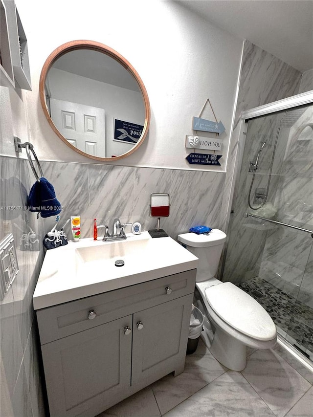 bathroom featuring toilet, marble finish floor, a stall shower, tile walls, and vanity