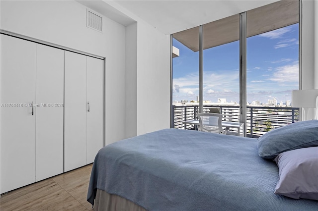 bedroom with visible vents, wood finished floors, access to exterior, expansive windows, and a view of city