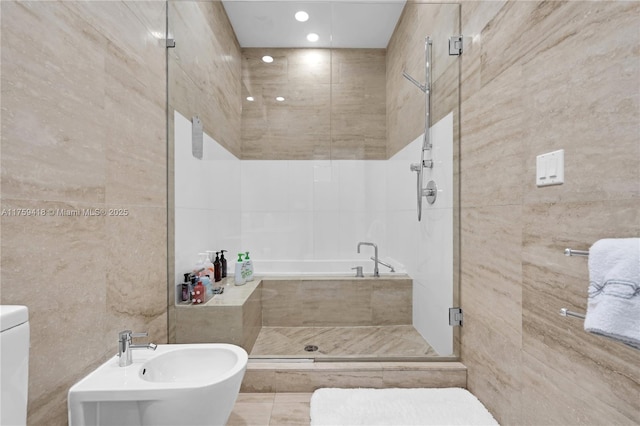 bathroom with tile walls, a bidet, a sink, and a shower stall