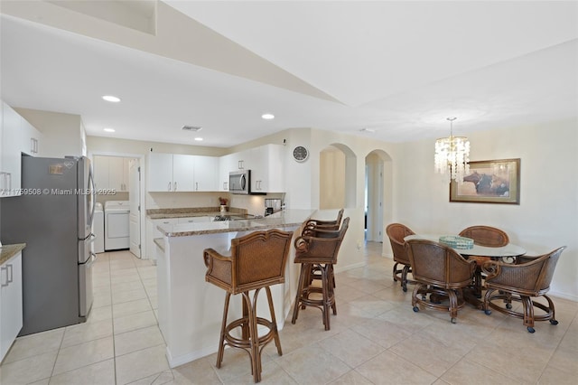 kitchen featuring arched walkways, appliances with stainless steel finishes, washer / clothes dryer, a peninsula, and light stone countertops