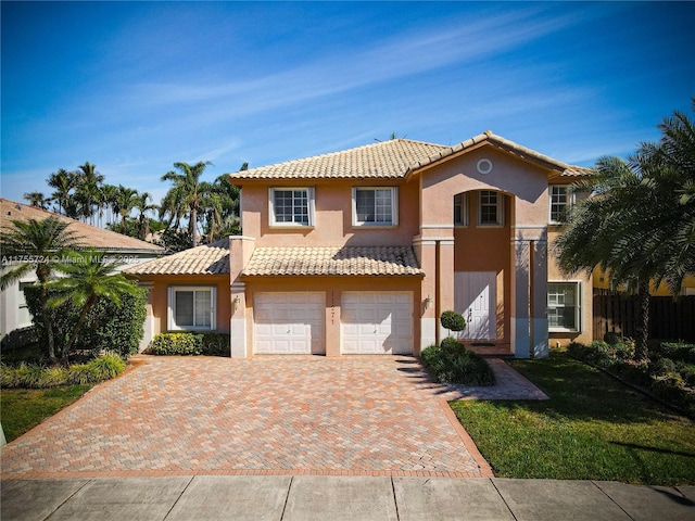 mediterranean / spanish house featuring decorative driveway, stucco siding, an attached garage, fence, and a tiled roof