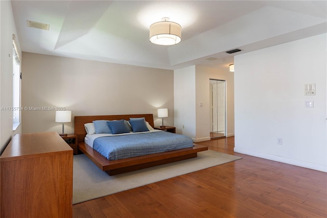 bedroom featuring hardwood / wood-style flooring, baseboards, visible vents, and a raised ceiling