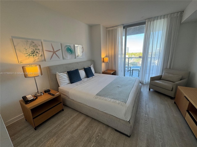 bedroom with expansive windows, wood finished floors, and access to exterior