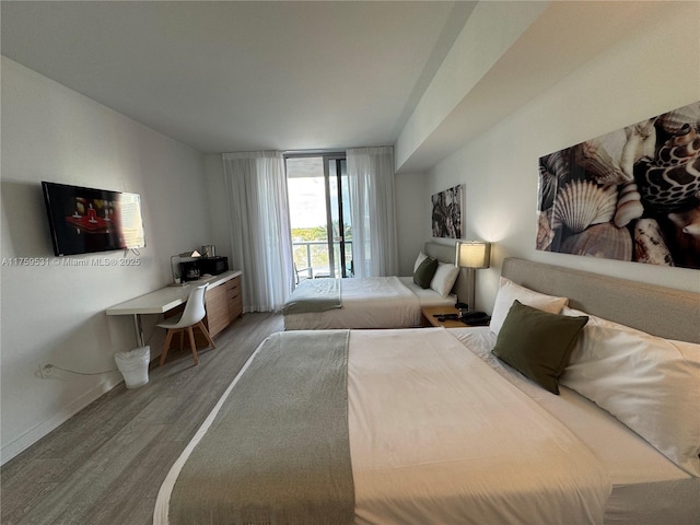 bedroom featuring access to exterior, expansive windows, baseboards, and wood finished floors