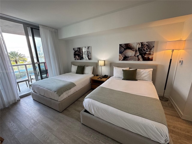 bedroom featuring baseboards, access to outside, floor to ceiling windows, and wood finished floors