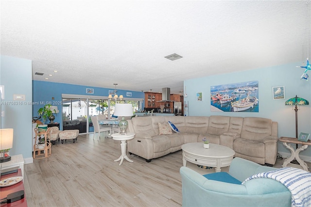 living area featuring a textured ceiling, wood finished floors, visible vents, and a notable chandelier