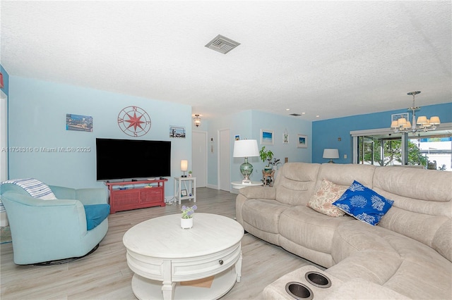 living area with a textured ceiling, wood finished floors, visible vents, and a notable chandelier