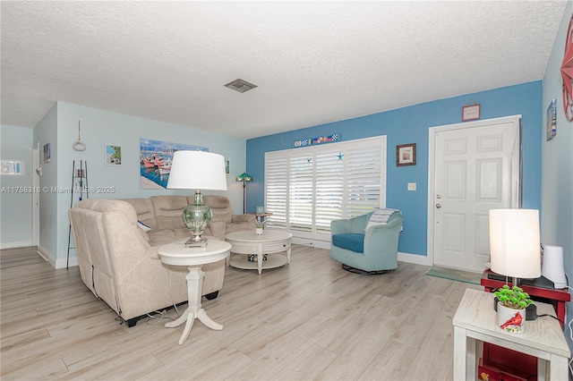 living room featuring light wood-type flooring, baseboards, visible vents, and a textured ceiling