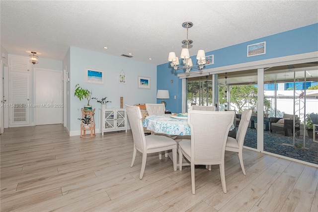 dining area featuring light wood finished floors, baseboards, a chandelier, and a textured ceiling