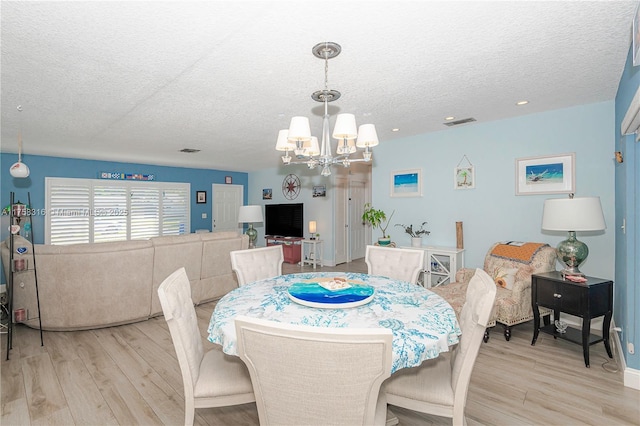 dining space featuring a chandelier, a textured ceiling, visible vents, and light wood-style floors