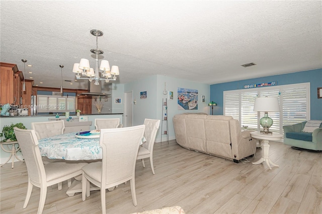 dining area featuring visible vents, light wood-style flooring, a textured ceiling, and an inviting chandelier