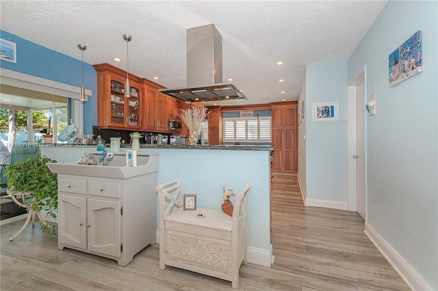 kitchen featuring island range hood, brown cabinetry, glass insert cabinets, stainless steel microwave, and a peninsula