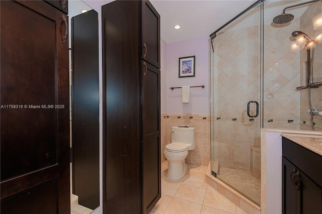 full bath with toilet, vanity, tile walls, a shower stall, and tile patterned floors