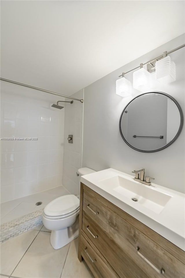 bathroom with tile patterned flooring, tiled shower, vanity, and toilet