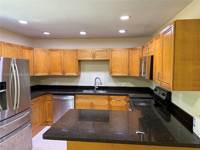 kitchen featuring a textured ceiling, stainless steel appliances, dark stone countertops, and a sink