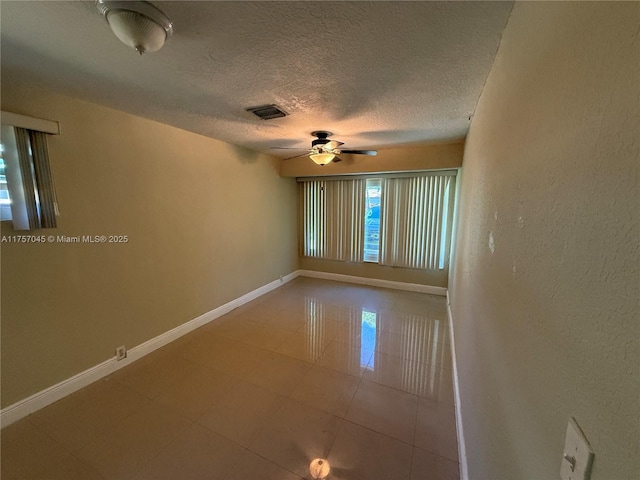 tiled empty room with a textured ceiling, a ceiling fan, visible vents, and baseboards