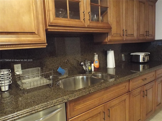 kitchen featuring dark stone counters, tasteful backsplash, stainless steel dishwasher, and a sink