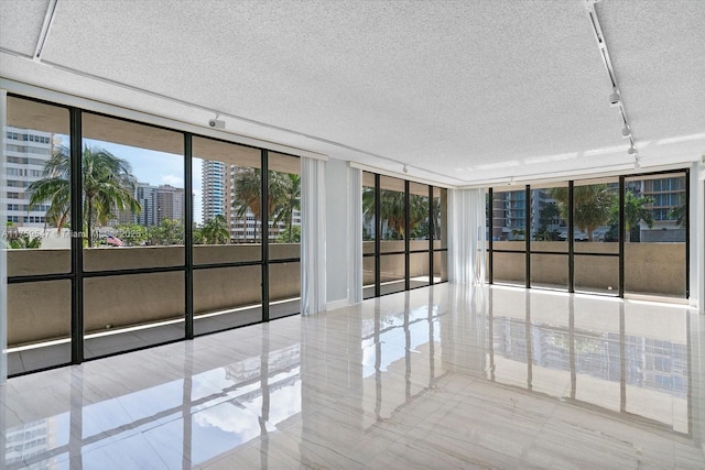 unfurnished room with a city view, floor to ceiling windows, a textured ceiling, and track lighting