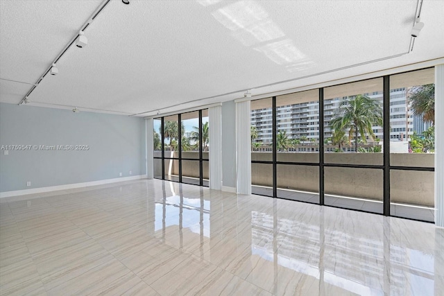 spare room with rail lighting, floor to ceiling windows, a textured ceiling, and baseboards