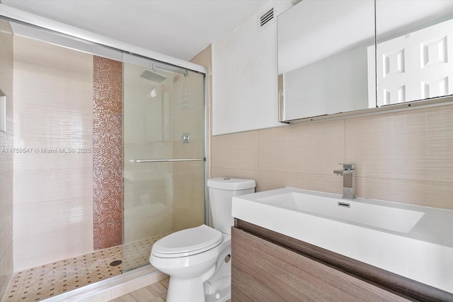 full bathroom featuring toilet, vanity, visible vents, tile walls, and a shower stall