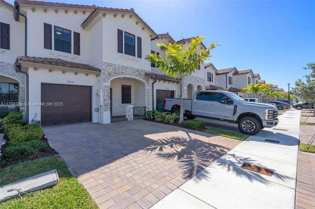 mediterranean / spanish-style house with stone siding, decorative driveway, an attached garage, and a tiled roof