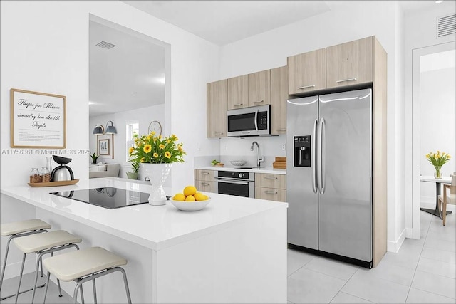 kitchen featuring light brown cabinets, visible vents, stainless steel appliances, light countertops, and a kitchen bar