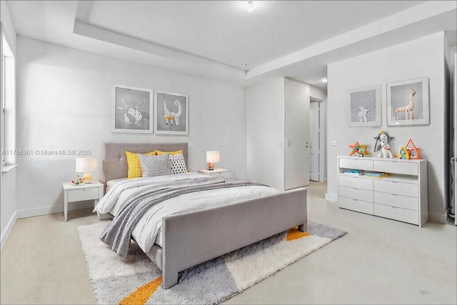 bedroom featuring a tray ceiling, baseboards, and concrete flooring